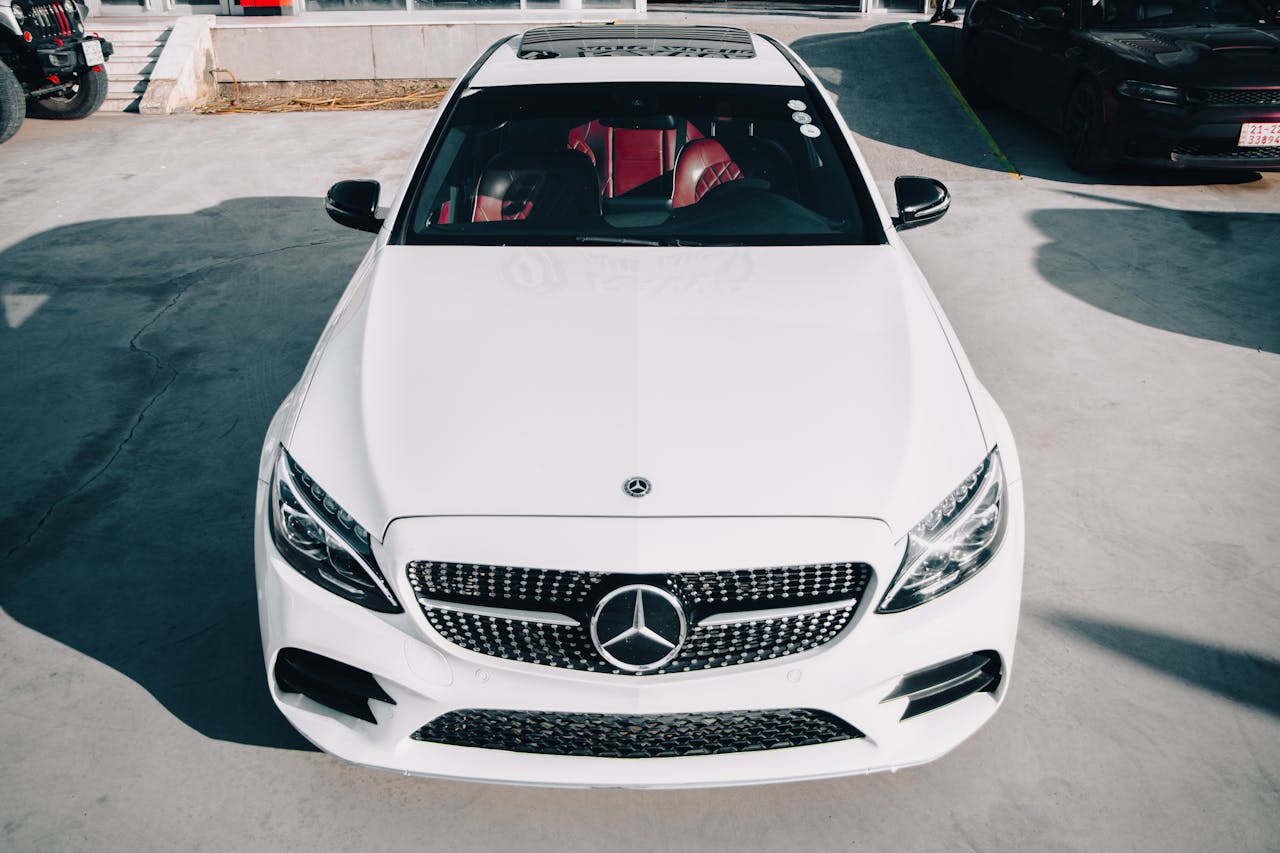 A high angle view of a white Mercedes Benz car in an outdoor sunlit parking area.